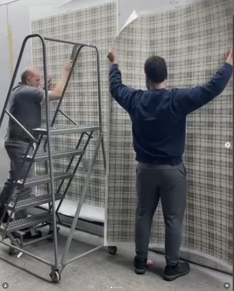 Two people working on a large wall with checkered wallpaper