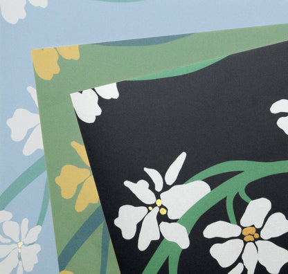 A close-up of patterned fabric or paper showing a black section with white flowers and green stems, layered over a light blue and green floral design.